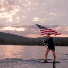 A person on a surfboard holding a flag and a flag